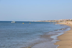 A beach with calm waters, a boat, and people enjoying the shore.