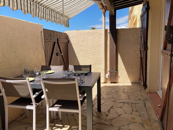 An outdoor patio with a table set for dining, stone flooring, and a wooden fence.