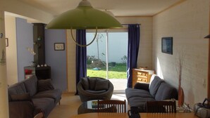 A living room with two sofas, a coffee table, a lamp, and a view of the outdoors through a glass door. - Villa, 300 m away, seaside, Agon-Coutainville, 7/8 people (Agon-Coutainville)