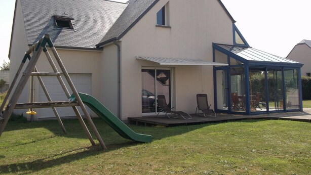 A house with a sloped roof, a covered patio area with chairs, and a green slide. - Villa, 300 m away, seaside, Agon-Coutainville, 7/8 people (Agon-Coutainville)