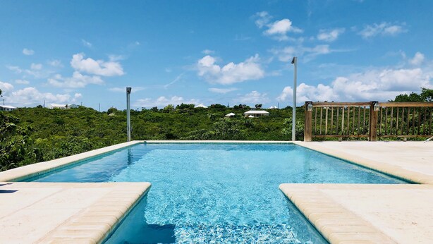 Uma piscina retangular com água azul cristalina, rodeada por um deck revestido com azulejos claros.