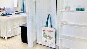 Quarto de hotel com cama, porta branca, prateleira com artigos de higiene pessoal e porta-toalhas.