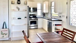 Uma cozinha moderna com armários brancos, eletrodomésticos de aço inoxidável e uma área de refeições com mesa e cadeiras de madeira.