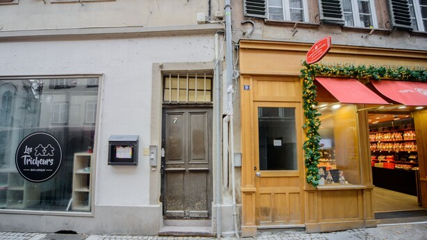 Une devanture de magasin avec une porte en bois et une vitrine où est affiché un panneau indiquant « Les Tricheurs, bar ludique ».