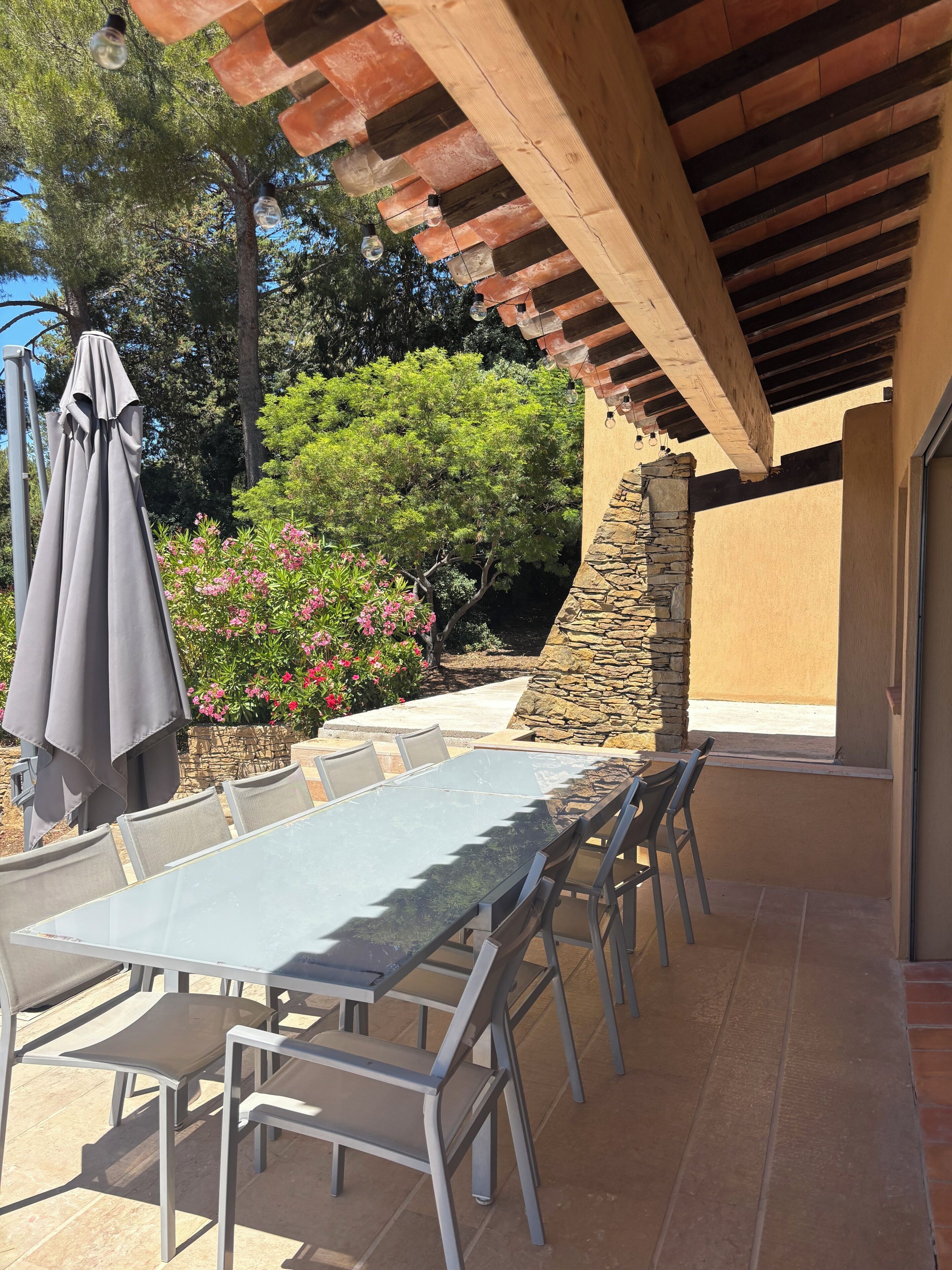 Une terrasse extérieure avec une table et des chaises, une pergola et un mur en pierre.