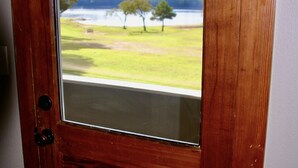 Puerta de madera con un ventanal que muestra una zona verde con árboles y una masa de agua.