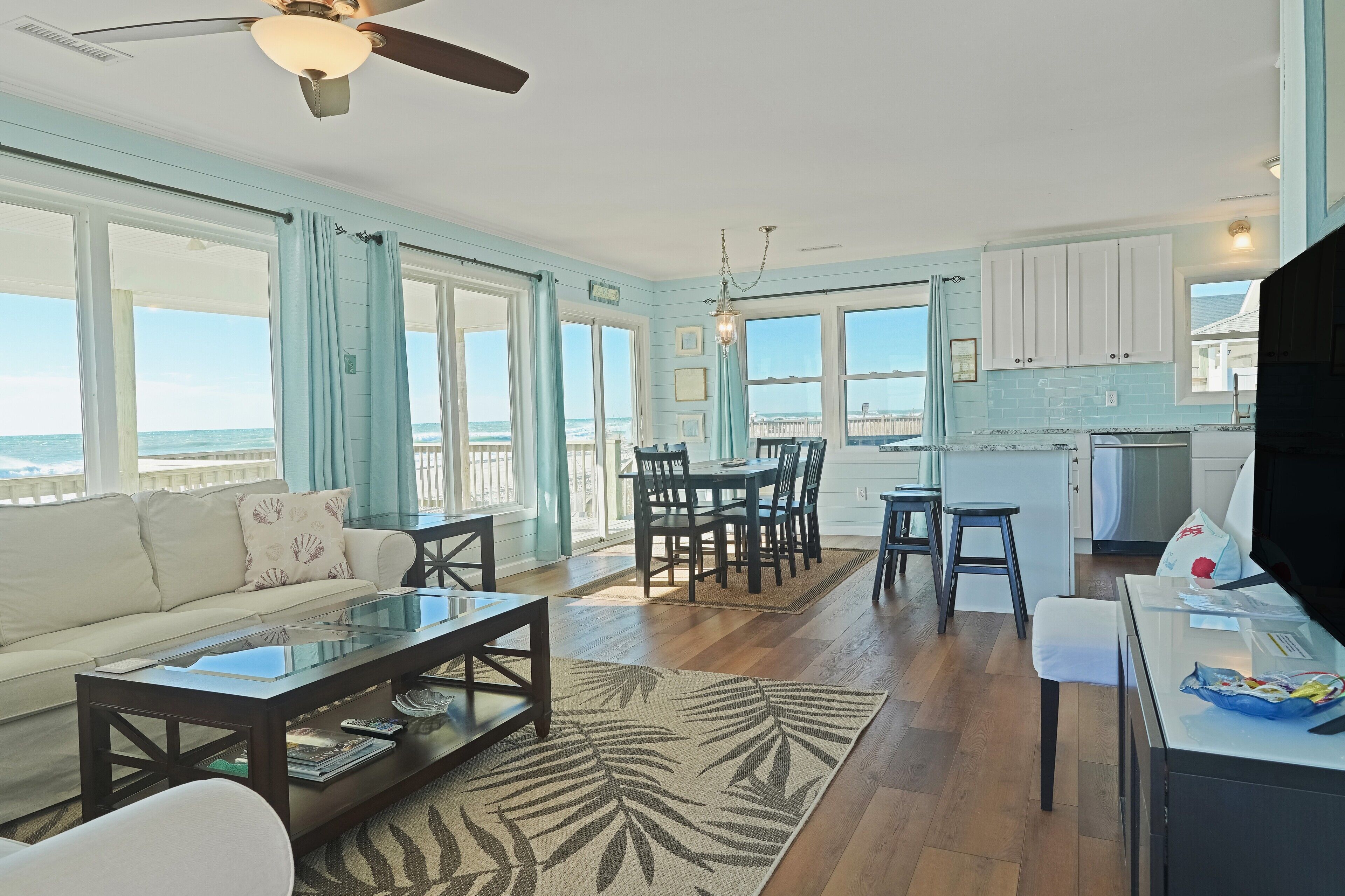 A spacious living room with a sofa, coffee table, and dining area. There is a view of the ocean through large windows.
