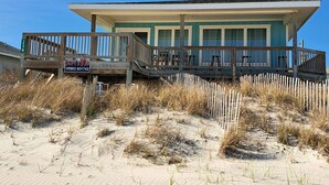 Ett hus vid stranden med en träveranda och en skylt med texten: ”Surf's Up VRBO 651742”.