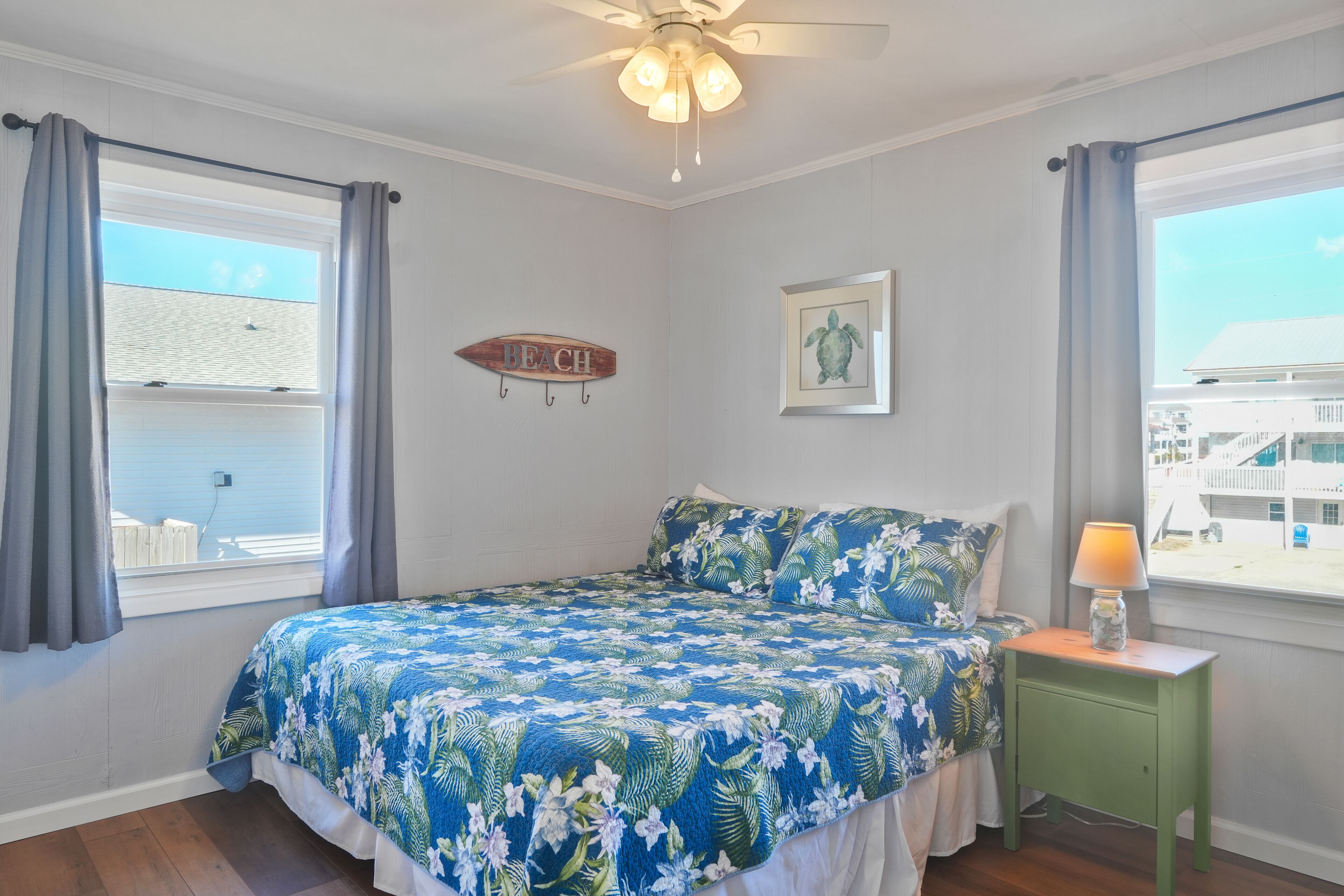 A bedroom with a bed, a nightstand, a ceiling fan, a window with curtains, and a wall-mounted picture.