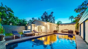 Un jardin avec une piscine, des chaises longues, une petite maison et des guirlandes lumineuses.