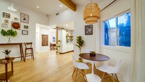 Une salle à manger spacieuse avec un plancher en bois, des chaises blanches et une table ronde. Des plantes en pot et des œuvres d’art ornent les murs.