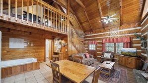 A log cabin interior with a dining area, sofa, TV, and a staircase to an upper level. - An Affair to Remember - 1BR/New Hot Tub/New Firepit/Grill/Perfect for 4 (Gatlinburg)