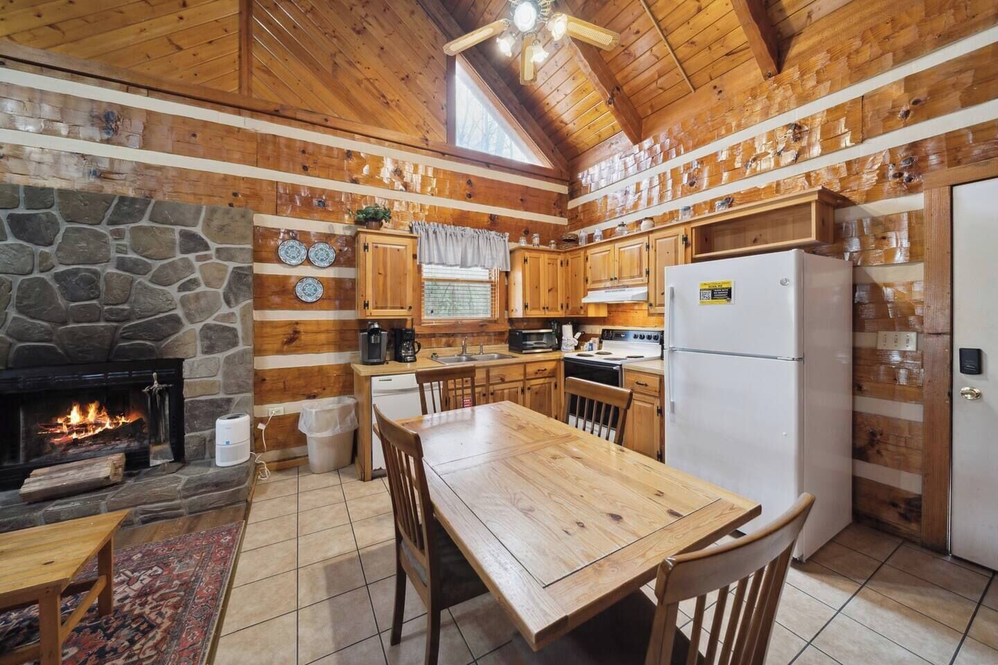 A rustic kitchen with a stone fireplace, wooden cabinets, and a tiled floor.