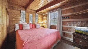 A cozy log cabin bedroom with a large bed, a television on a wooden dresser, and framed leaf artwork on the walls. - An Affair to Remember - 1BR/New Hot Tub/New Firepit/Grill/Perfect for 4 (Gatlinburg)