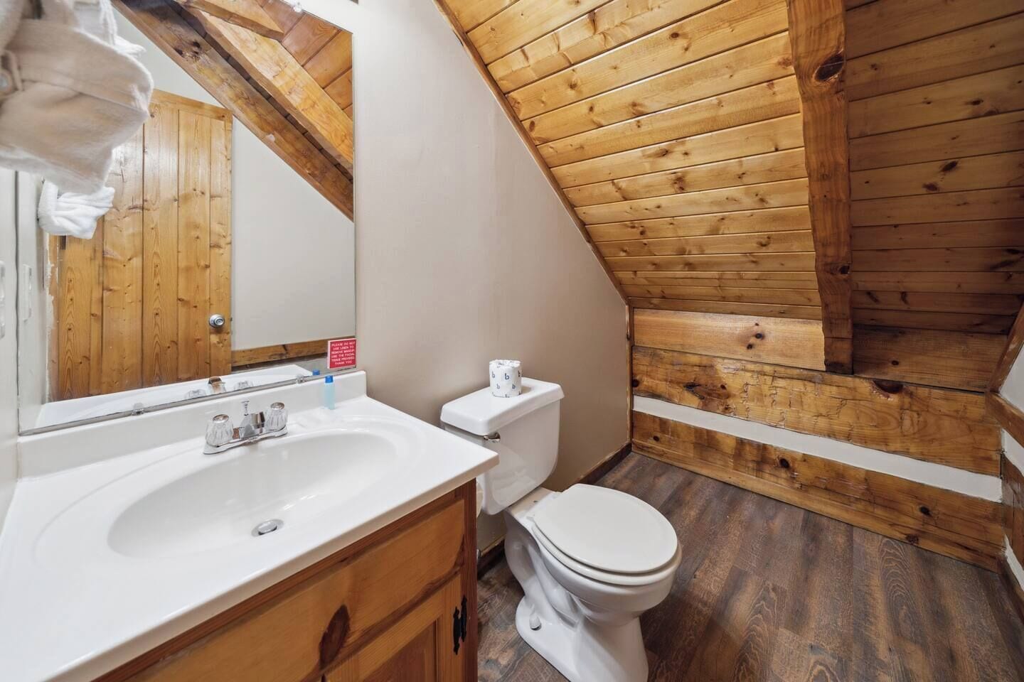 Une petite salle de bain aux murs lambrissés, avec un lavabo, des toilettes et un miroir, le tout de couleur blanche.
