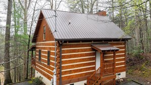 A log cabin with a metal roof, wooden exterior, and a small porch with steps. - An Affair to Remember - 1BR/New Hot Tub/New Firepit/Grill/Perfect for 4 (Gatlinburg)
