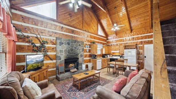 A cozy cabin interior with a stone fireplace, wooden furniture, and a kitchen area. - An Affair to Remember - 1BR/New Hot Tub/New Firepit/Grill/Perfect for 4 (Gatlinburg)