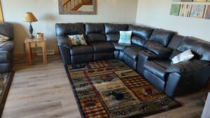 Ein Wohnzimmer mit einem Ecksofa, einem kleinen Holztisch, einem gemusterten Teppich und Wandbildern.