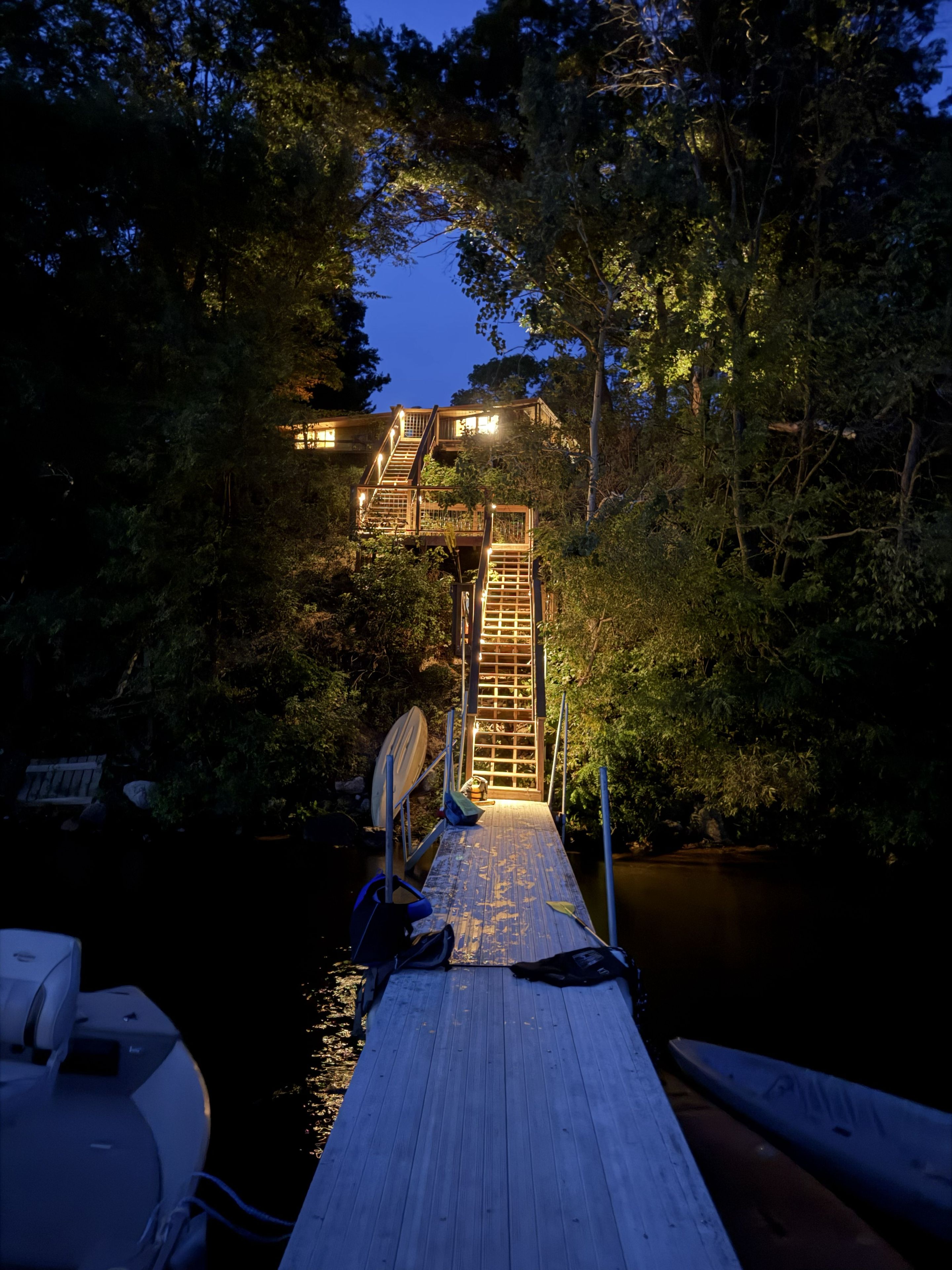 Une jetée en bois menant à un bâtiment doté d’un escalier, le tout entouré d’arbres et bordé par une étendue d’eau.