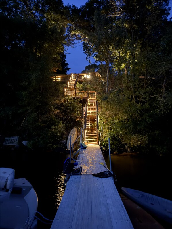 A wooden dock leading to a building with a staircase, surrounded by trees and a body of water.