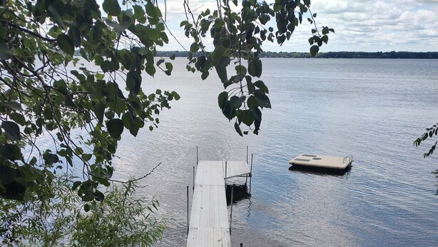 Eine Holzterrasse führt zu einem Steg über ruhigem Wasser, umgeben von viel Grün.