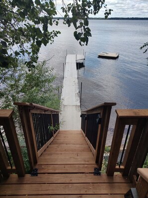 A wooden deck leading to a dock over calm water, surrounded by greenery.