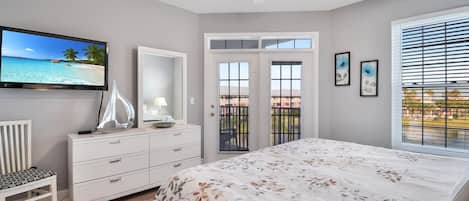 A bedroom with a bed, a dresser, a television, a ceiling fan, and a balcony with a view.