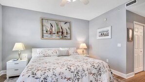 A bedroom with a bed, two bedside tables, a nightstand, a painting, and a door. - Atlantis 302D - Steps to the Ocean (St Augustine Beach)