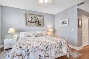 A bedroom with a bed, two bedside tables, a nightstand, a painting, and a door. - Atlantis 302D - Steps to the Ocean (St Augustine Beach)