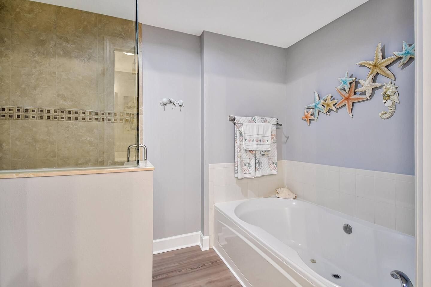 Une salle de bain avec une baignoire, une cabine de douche en verre et des décorations murales représentant des étoiles de mer.