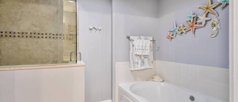 Une salle de bain avec une baignoire, une cabine de douche en verre et des décorations murales représentant des étoiles de mer.