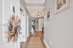 A hallway with a wooden floor, white walls, and a door with a decorative wall hanging.
