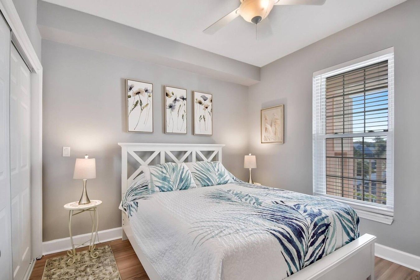 Un dormitorio con cama, ventilador de techo, ventana con persianas y decoración en la pared.