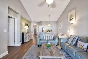 A living room with a blue sofa, a wooden coffee table, and a kitchen in the background.