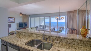 A kitchen with granite countertops, stainless steel sink, and a large window overlooking a balcony with outdoor seating. - 8th floor beach front condo in Tides @ Tops'l (Miramar Beach)