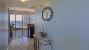A hallway with a view to a balcony, a round mirror on the wall, and a small table with a ship model. - 8th floor beach front condo in Tides @ Tops'l (Miramar Beach)