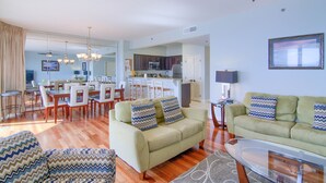 A spacious living room with a sofa, a glass coffee table, and a dining area with chairs and a table. - 8th floor beach front condo in Tides @ Tops'l (Miramar Beach)