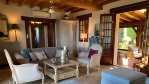 Una sala de estar acogedora con un sofá, sillones, pufs, una mesa de centro y vista al jardín a través de un ventanal.