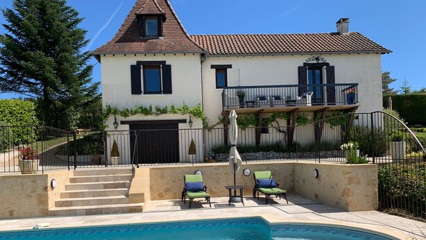 Una casa de dos pisos con piscina, mobiliario exterior y un jardín bien cuidado.