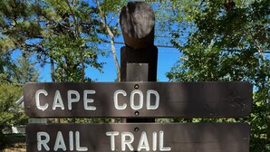 Ein Wegweiser mit Pfeilen und Beschriftungen, die den Weg zum Cape Cod Rail Trail, der Cape Cod National Seashore sowie nach Brewster, Harwich, Dennis und dem Chatham Connector Trail anzeigen.