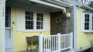 Ein gelbes Haus mit Veranda, weißen Fensterläden, einem weißen Geländer und einem Kranz an der Wand.