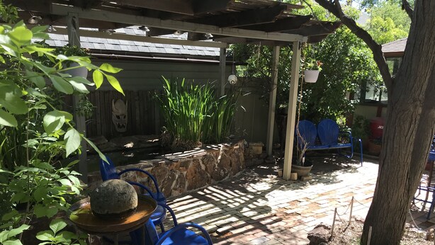A covered patio area with a stone wall, potted plants, and blue chairs.