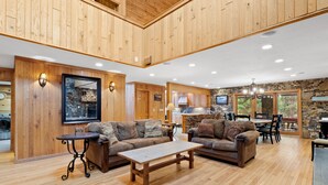 A spacious living area with wooden flooring, two sofas, a coffee table, and a stone accent wall. - Beautiful 6 Bed/4.5 Bath - Close To 7 Springs & Laurel Highlands Attractions (Champion)