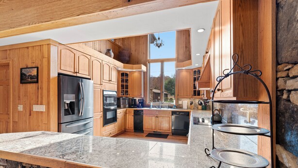 A modern kitchen with wooden cabinets, granite countertops, and a stone wall. - Beautiful 6 Bed/4.5 Bath - Close To 7 Springs & Laurel Highlands Attractions (Champion)