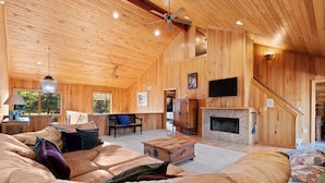A spacious living room with a large sofa, a wooden coffee table, and a fireplace. There is a television mounted on the wall and a ceiling fan. - Beautiful 6 Bed/4.5 Bath - Close To 7 Springs & Laurel Highlands Attractions (Champion)