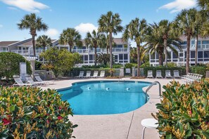 A swimming pool with lounge chairs, palm trees, and a building with balconies in the background.