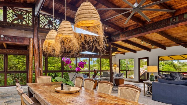 A spacious dining area with a large wooden table, wicker chairs, and hanging rope lights. - Tiki Home - Unique Custom Home Steps to the Beach and Town (Hanalei)