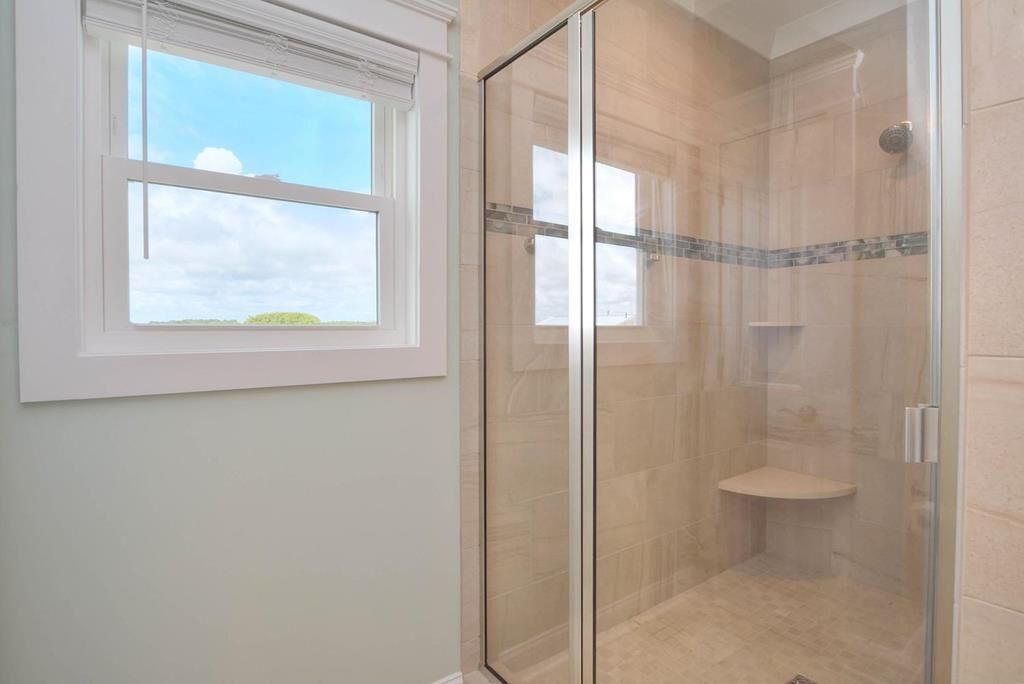 A glass-enclosed shower with a tiled floor and a small shelf.