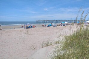 A beach with a pier, tents, and beachgoers.