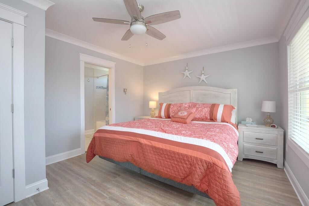 Une chambre à coucher comprenant un lit, une table de chevet, un ventilateur de plafond, une porte et une fenêtre avec des stores.
